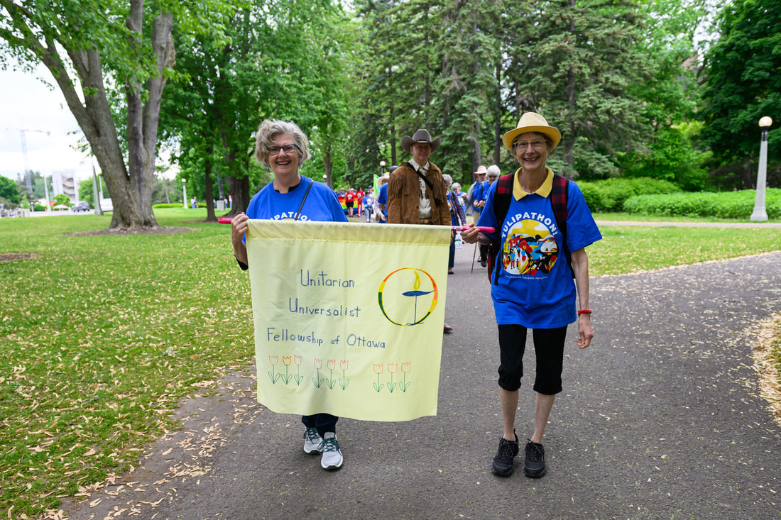 Two UUFO members carrying a hand-painted fabric banner with Unitarian Universalist Fellowship of Ottawa, the rainbow chalice, and some tulips